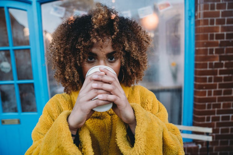 A woman in a yellow sweater enjoys a cup of coffee outside.