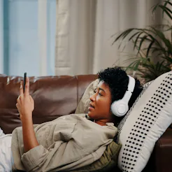 A woman with headphones on selects a binaural beats playlist for migraine. A doctor explains why bin...