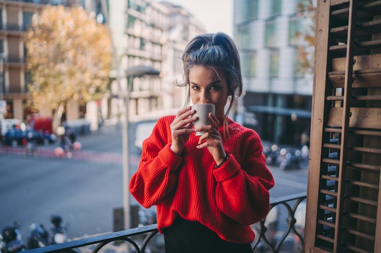 A woman enjoys a cup of coffee on her balcony in the fall. 