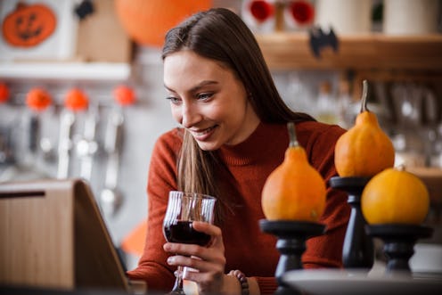 A woman looks at a tablet on a stand. she's surrounded by pumpkins and bats and other spooky hallowe...