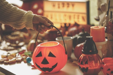 A young woman holds the handle of a pumpkin bucket surrounded by Halloween decor and goodies.