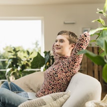 A woman with short hair sits on a white couch surrounded by plants. This article details 7 signs of ...