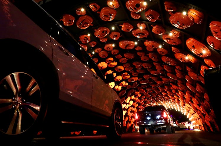 Cars stop in a pumpkin tunnel of a Halloween drive-thru event.