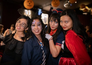 A group of women in Halloween costumes stand under hanging pumpkins. 