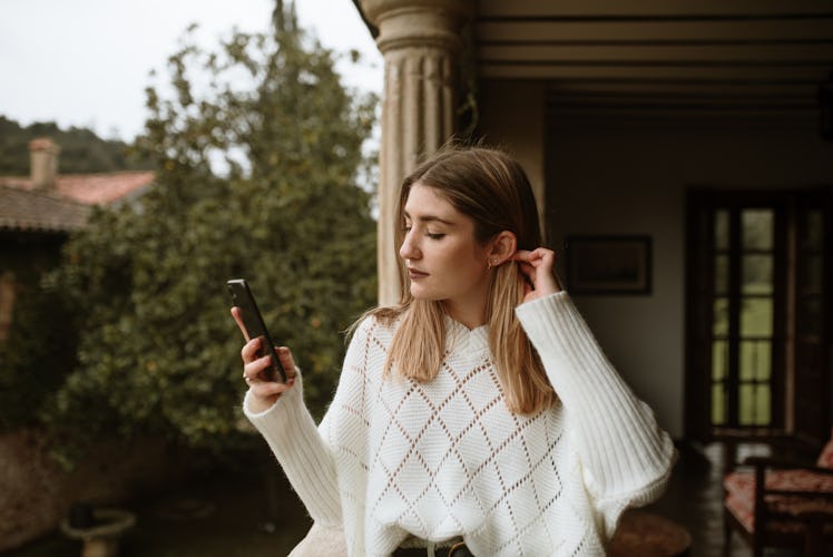 A with anxiety in a white sweater standing on a terrace and texting her crush