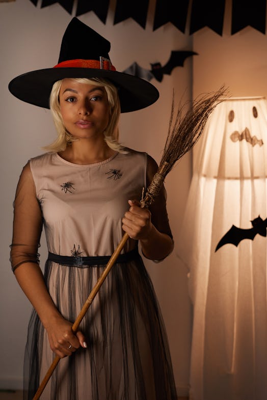 A young Black woman dressed up like a witch poses for a picture in her home.