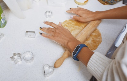 A young woman rolls out sugar cookie dough on a counter with a rolling pin.