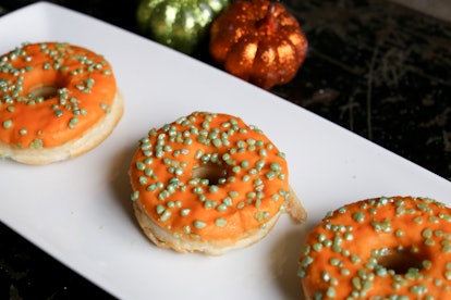 A tray of orange doughnuts sits on the table with mini pumpkins. 