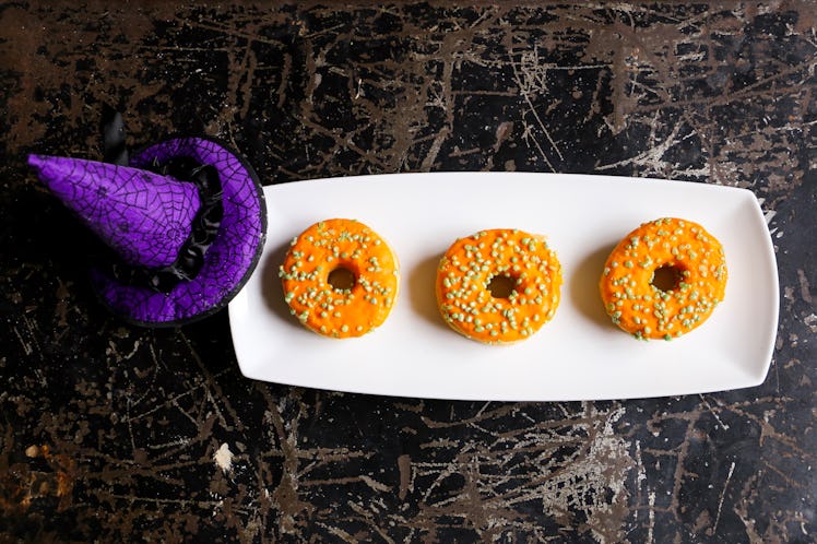 A plate with three Halloween orange doughnuts sits on the counter next to a purple witch's hat. 