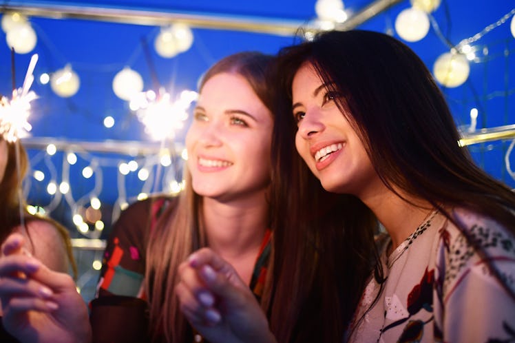 Two happy friends hold up sparklers outside at night.