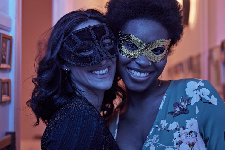 Two friends smile with costume masks on their faces. 