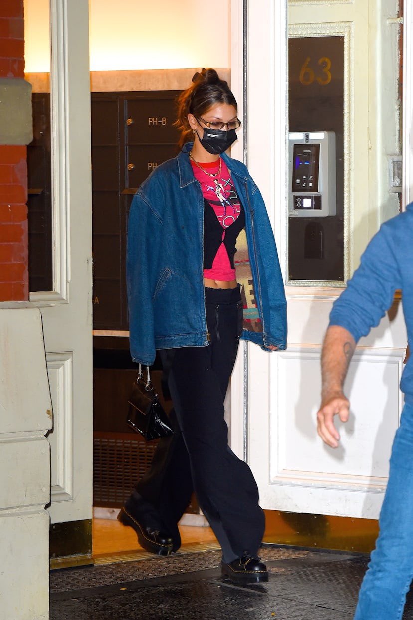 Bella Hadid walking dressed in a graphic tee, cardigan, and oversized denim jacket on top