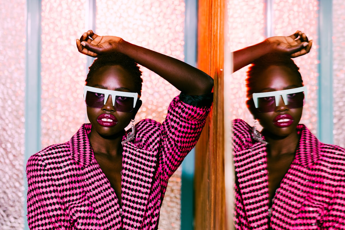 A young, fashionable Black woman poses in a black and pink blazer against a mirror for a fashion mag...