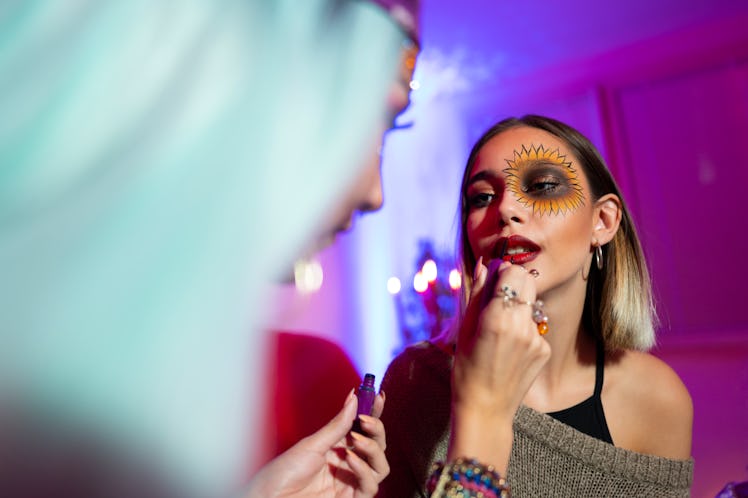 A young woman puts costume makeup on her friend for Halloween.
