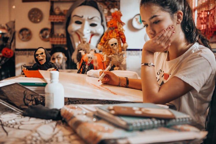 A young woman draws with an orange marker while sitting near Halloween decorations.