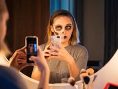 A young woman wearing Halloween makeup poses in her bathroom mirror for a selfie.