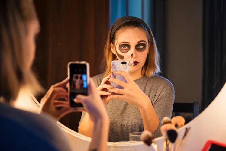 A young woman wearing Halloween makeup poses in her bathroom mirror for a selfie.