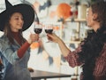 Two women dressed up for Halloween cheers with their wine glasses in the kitchen. 