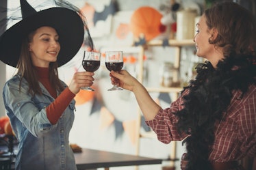 Two women dressed up for Halloween cheers with their wine glasses in the kitchen. 