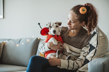 A young woman sits with her dog on the couch while they're both wearing Halloween costumes.
