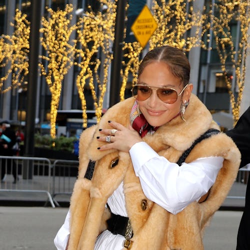 Jennifer Lopez with sunglasses on, wearing a white dress and a fur vest while walking on the street