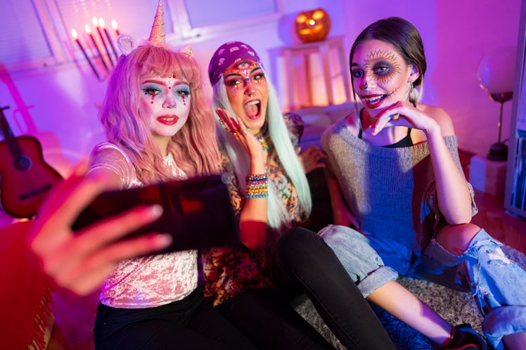 Three friends dressed up for Halloween record a video on their phone. 