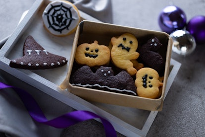 Some Halloween cookies made to look like ghosts and bats sit in a box on the table. 