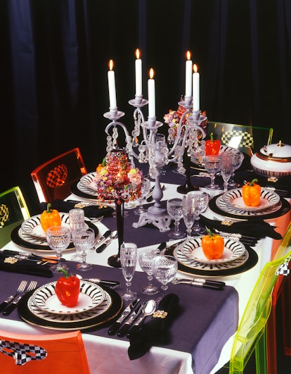 A Halloween dinner table is set with black napkins, black and white plates, candles, and face masks ...