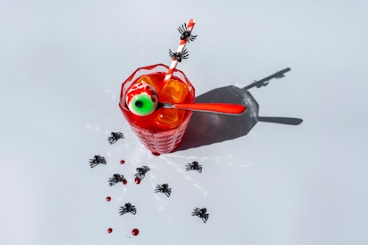 A Halloween cocktail sits on a countertop surrounded by plastic spiders.