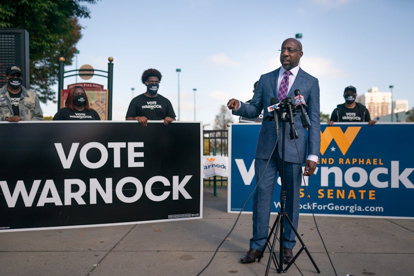 Rev. Raphael Warnock giving a speech, with signs that say "Vote Warnock" behind him.