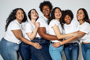 A group of woman all wearing white t-shirts and blue jeans huddle up. 