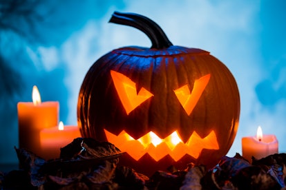 A jack-o'-lantern sits on a pile of leave next to a candle. 