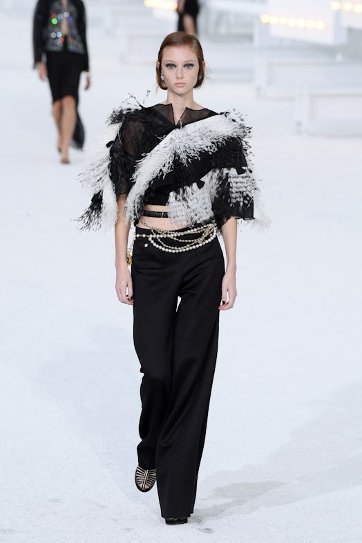 A model wears wide-leg pants paired with a black-and-white feather embellished crop top from Chanel'...