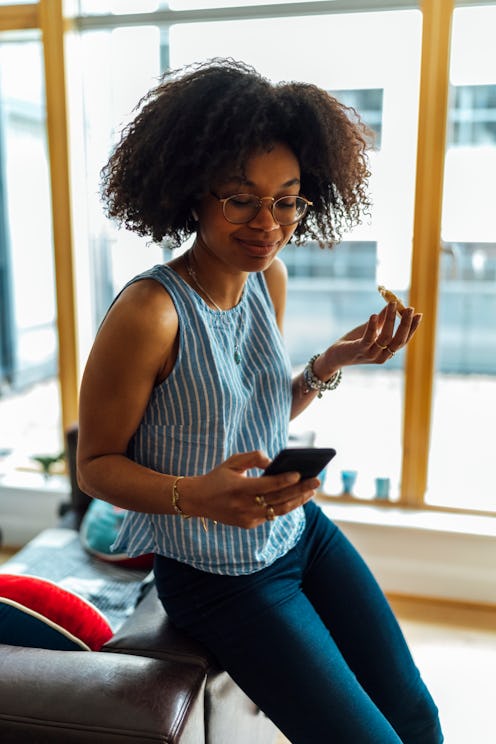 A woman with natural hair and glasses smiles at her phone while reading real-life embarrassing Inst...