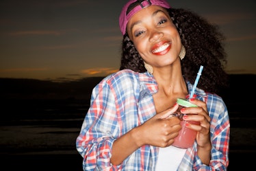 A happy woman wearing a backwards baseball cap and flannel shirt holds a mason jar with a wine slush...