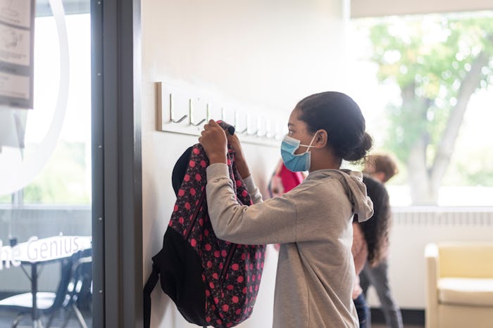 girl hanging up backpack wearing face mask