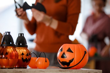 A pumpkin bucket sits on the table, as a woman cuts a bat decoration in the kitchen. 