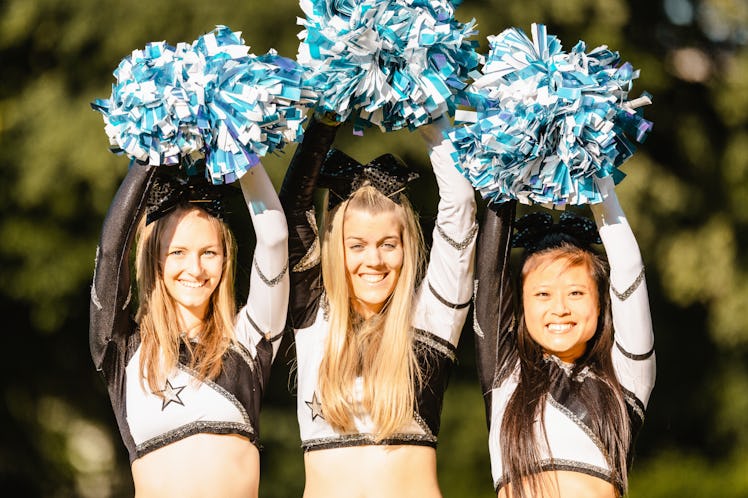 Three cheerleaders raise their pom poms over their heads.