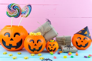An assortment of plastic jack-o-lanterns, filled with candy, sits on a table next to a pink wall. 
