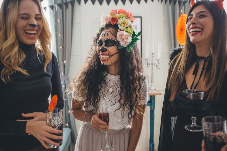 Three sorority sisters laugh while enjoying drinks and dressed up for Halloween.