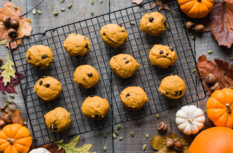 Pumpkin spice cookies with chocolate chips sit on a rack with pumpkins and fall leaves surrounding i...