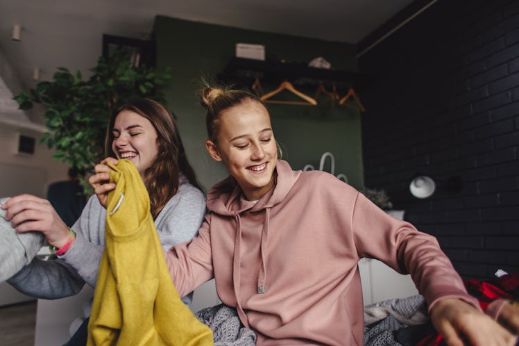 Two young women wearing sweatshirts sit on a bed while looking at their new fall sorority gear.