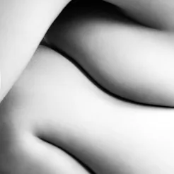 A closeup of a woman's breasts folded over her knees. This article explains early signs of breast ca...