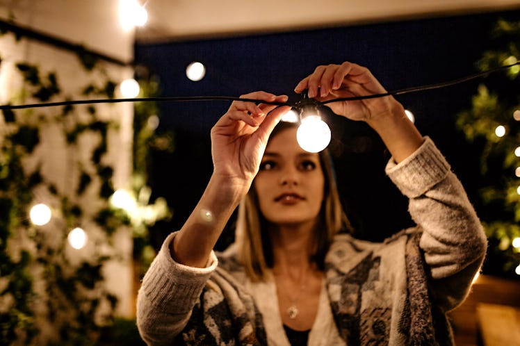 A woman hangs up string lights on her balcony in the winter.