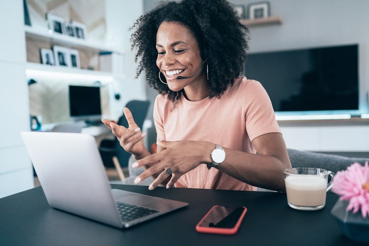 A happy woman laughs while talking to someone on her laptop via video chat in her apartmenr.