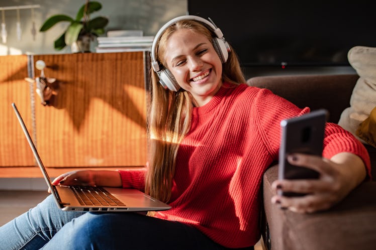 A young woman wearing a red sweater takes a selfie on her phone while participating in an online exp...