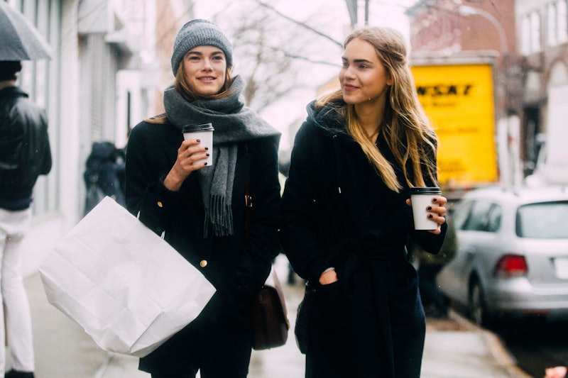 Two young female friends walking down the street in black winter coats and coffees to go