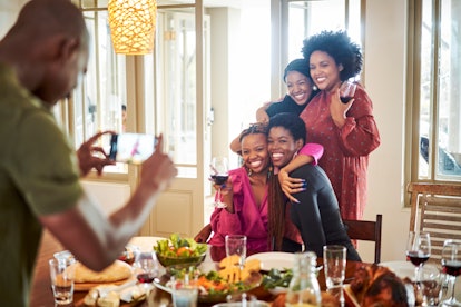 A group of happy women pose for a picture at their Friendsgiving dinner table.