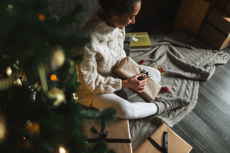 A woman wraps presents for Christmas, while sitting next to her tree.