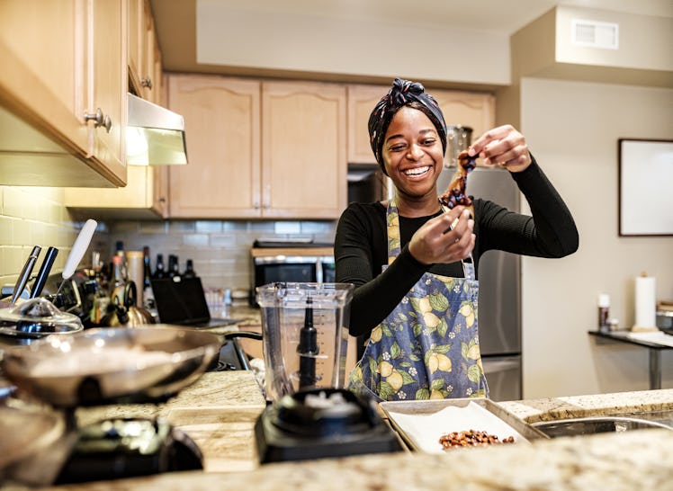 A happy woman cooks in her kitchen, while wearing a lemon and blue apron. 